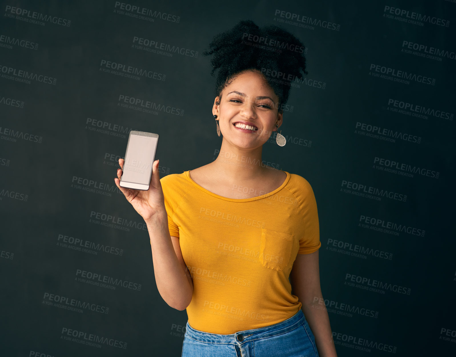 Buy stock photo Shot of a young woman holding a cellphone while posing against a grey background