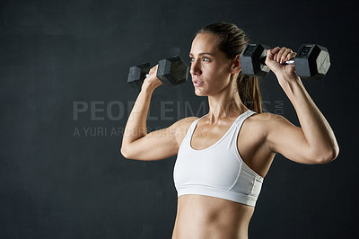 Buy stock photo Studio shot of an attractive young woman working out with dumbbells against a dark background