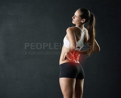 Buy stock photo Studio shot of a sporty young woman holding her lower back in pain against a dark background