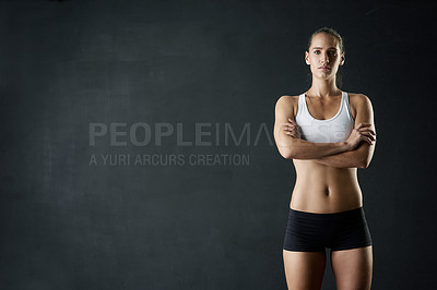 Buy stock photo Studio portrait of a sporty young woman standing with her arms folded against a dark background