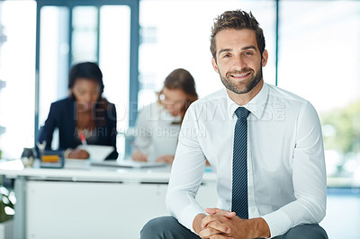 Buy stock photo Portrait of a young businessman sitting in an office with colleagues in the background