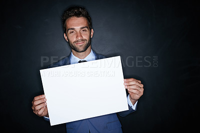 Buy stock photo Studio portrait of a handsome young man holding a blank placard against a dark background