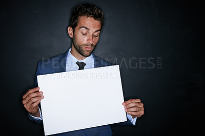 Buy stock photo Studio shot of a handsome young man holding a blank placard against a dark background