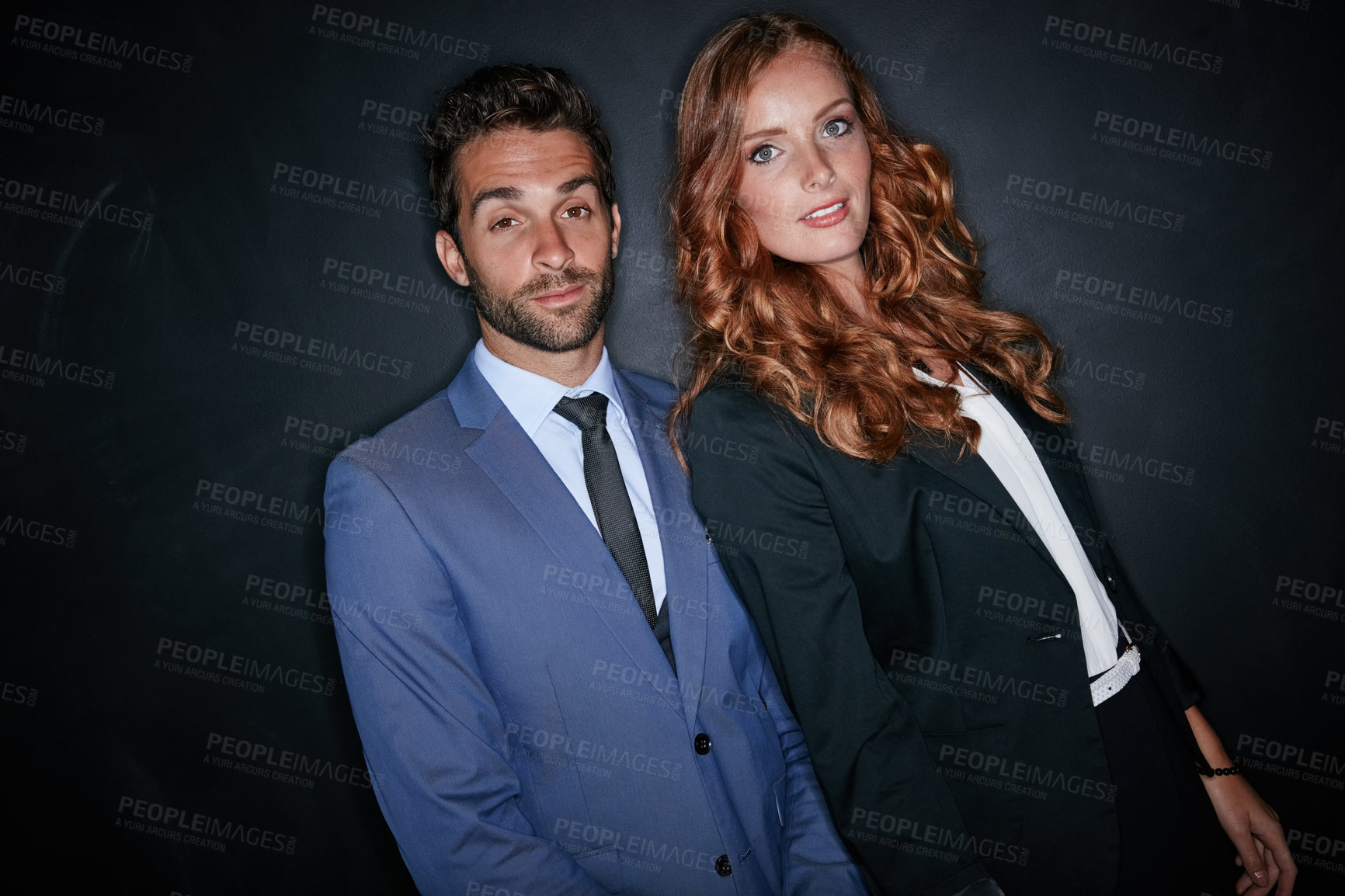 Buy stock photo Studio portrait of a young couple standing against a dark background