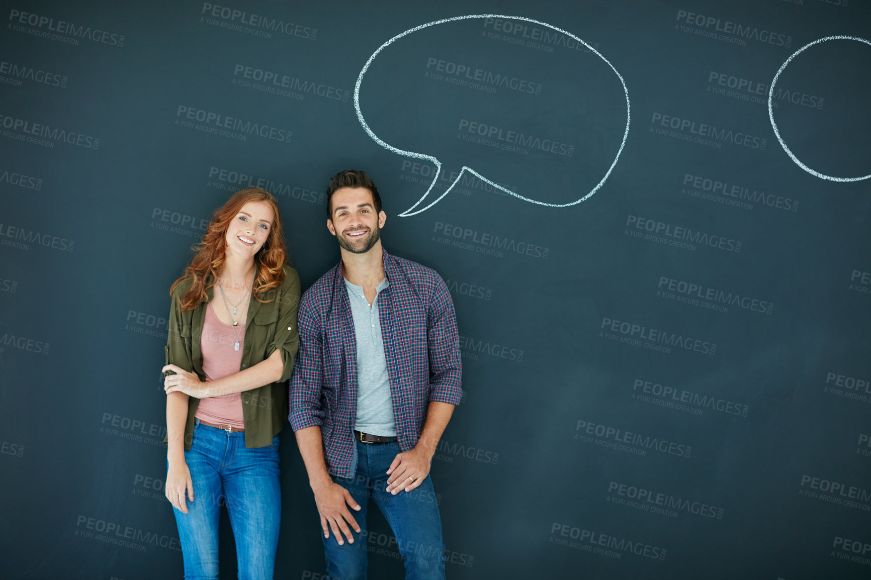 Buy stock photo Portrait of a young couple standing in front of a blackboard with speech bubbles drawn on it