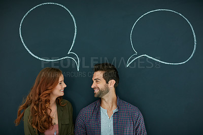 Buy stock photo Shot of a young couple standing in front of a blackboard with speech bubbles drawn on it