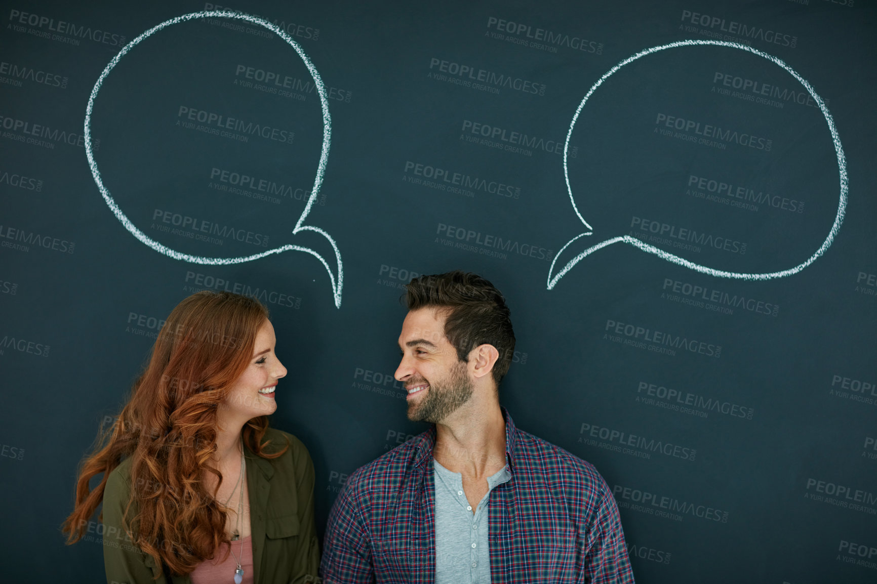 Buy stock photo Shot of a young couple standing in front of a blackboard with speech bubbles drawn on it