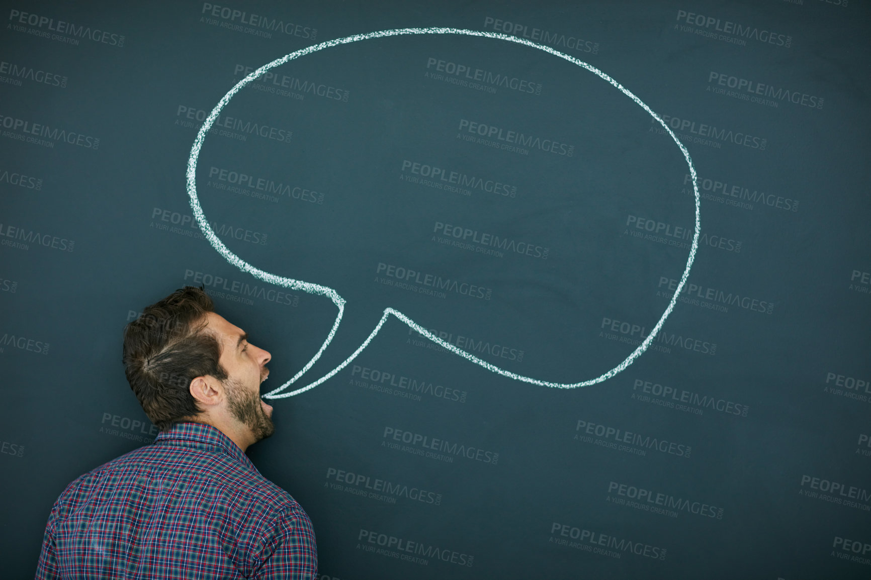 Buy stock photo Shot of a young man standing in front of a blackboard with a speech bubble drawn on it