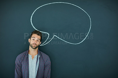 Buy stock photo Portrait of a young man standing in front of a blackboard with a speech bubble drawn on it