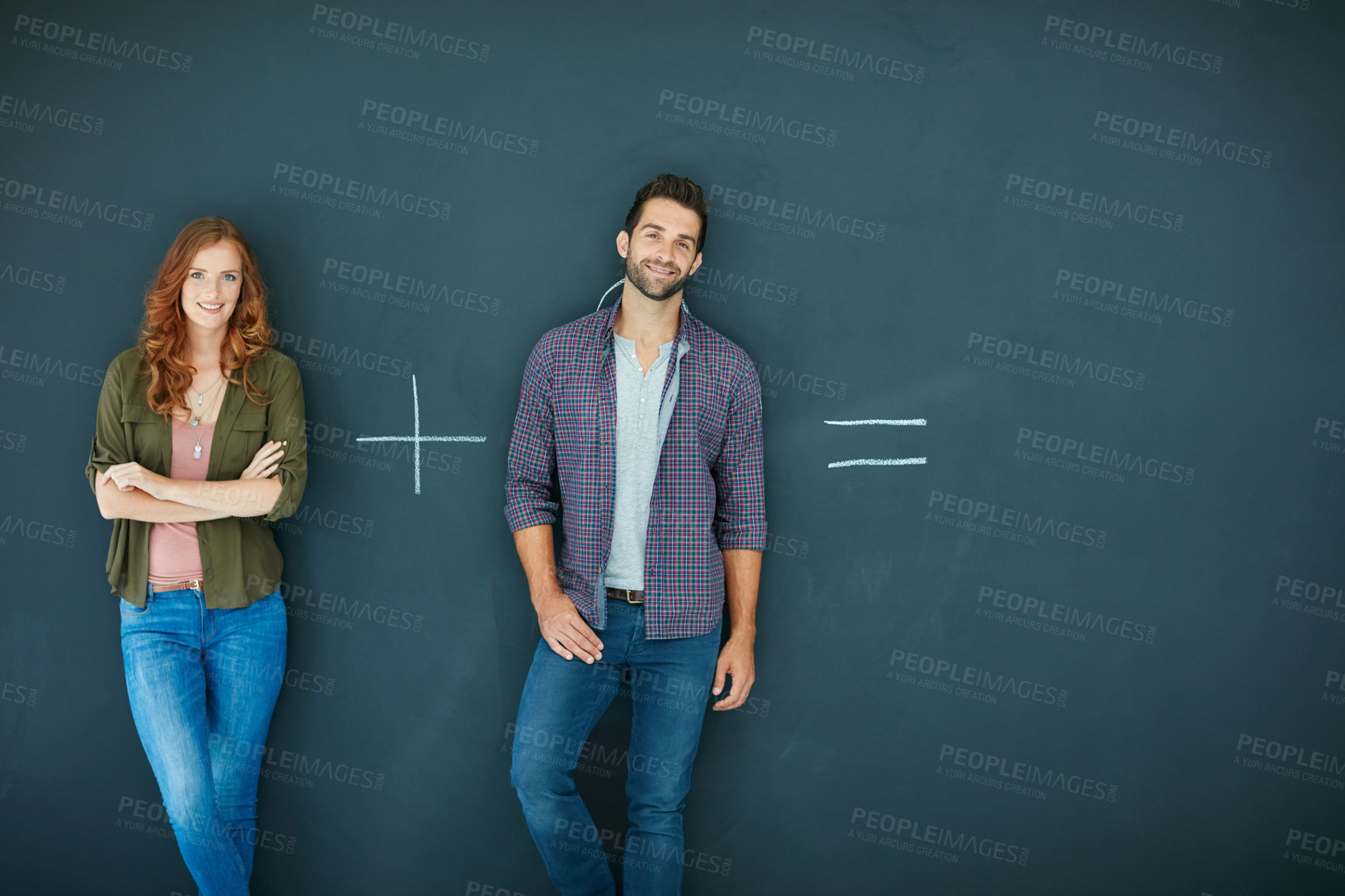 Buy stock photo Shot of a young couple standing in front of a blackboard with symbols written on it