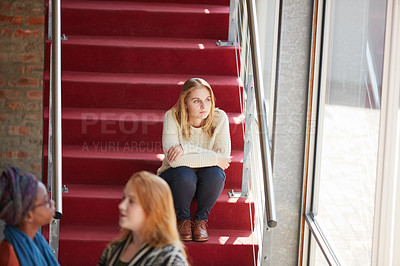 Buy stock photo Cropped shot of a university student sitting alone amongst her peers on campus