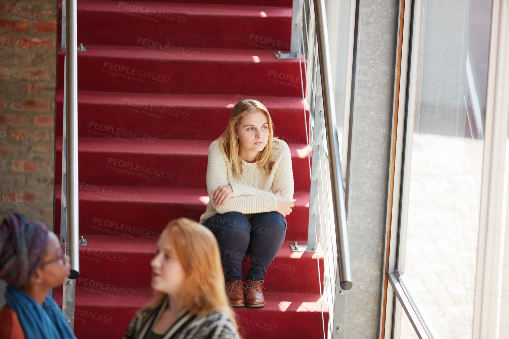 Buy stock photo Cropped shot of a university student sitting alone amongst her peers on campus