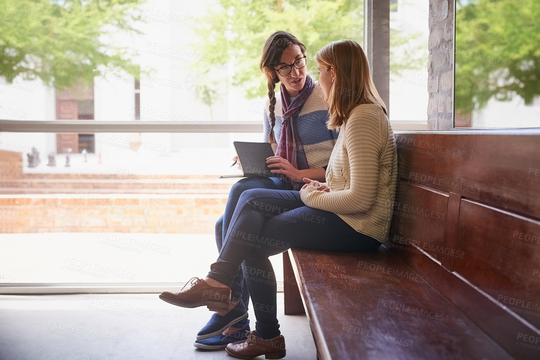 Buy stock photo Shot of two university students looking through some notes together on campus