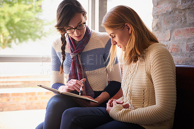 Buy stock photo Shot of two university students looking through some notes together on campus