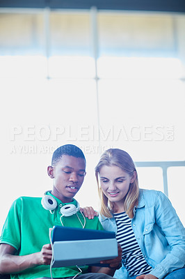Buy stock photo Shot of two university students looking at a digital tablet while sitting in their classroom