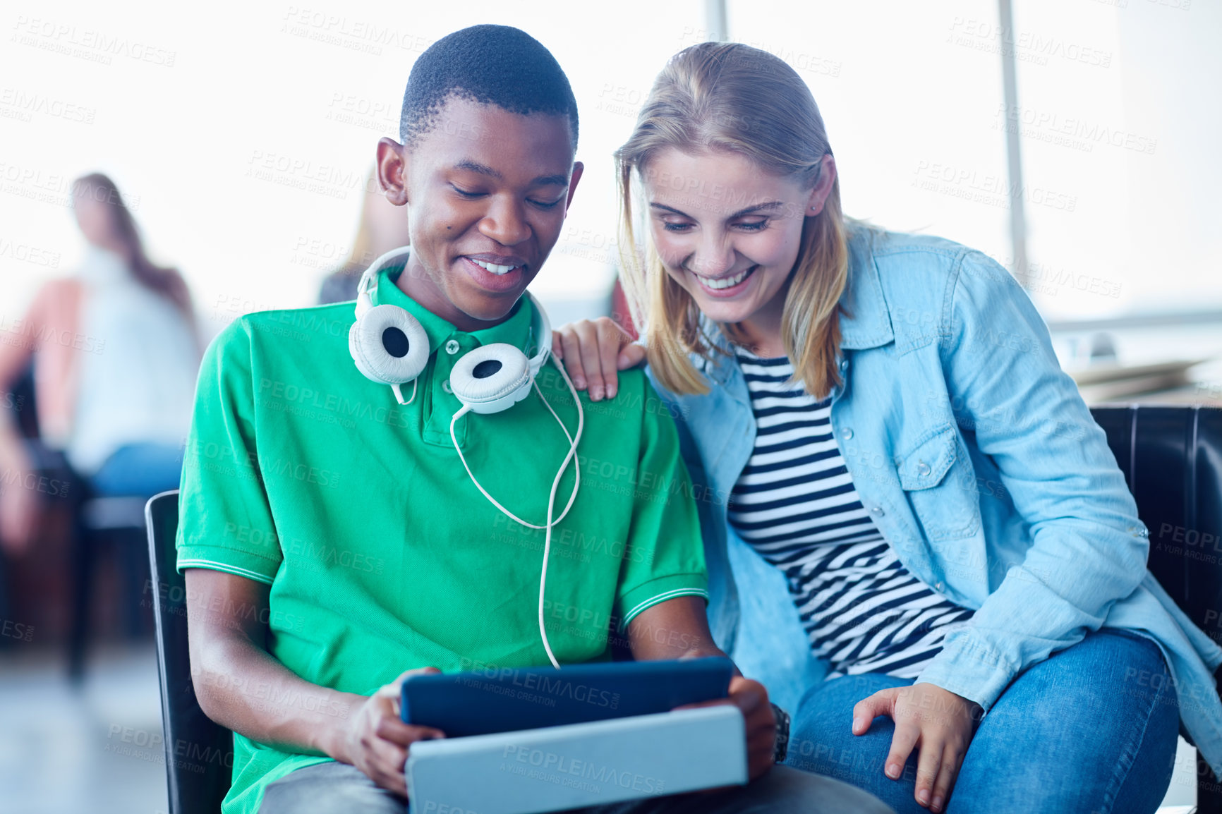 Buy stock photo Shot of two university students looking at a digital tablet while sitting in their classroom