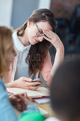 Buy stock photo Shot of a worried looking university student reading a text message in class