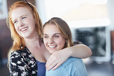 Buy stock photo Shot of two university students embracing while standing in their classroom