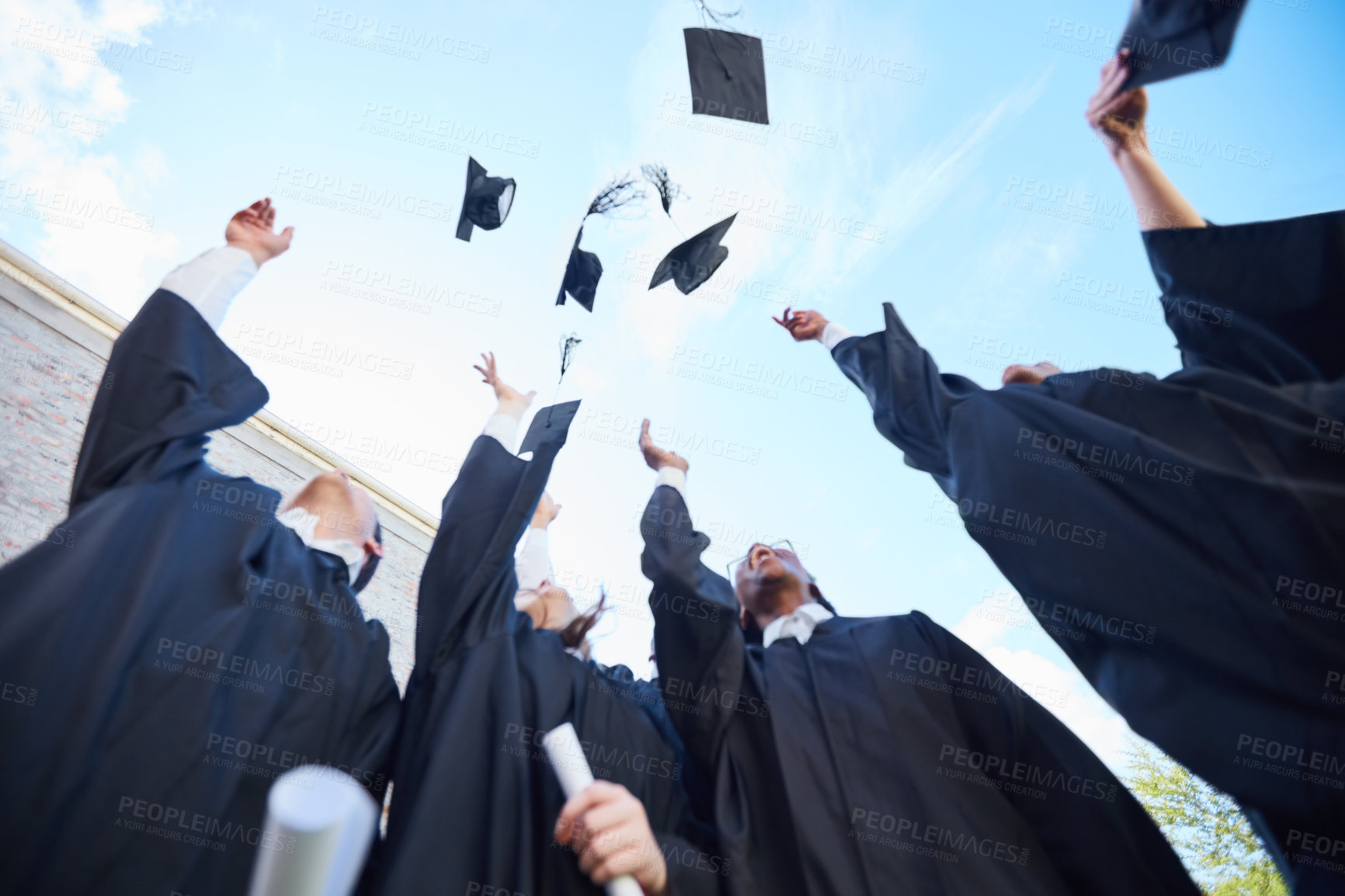 Buy stock photo Low angle shot of a group of students throwing their caps into the air on graduation day