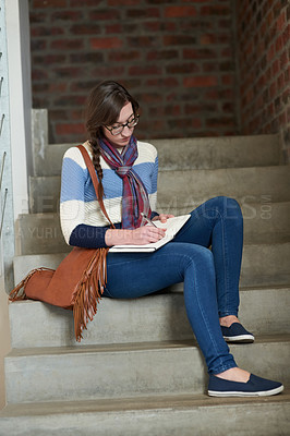 Buy stock photo Shot of a university student writing in her notebook on campus