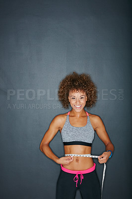 Buy stock photo Portrait of a sporty young woman measuring her waist against a grey background