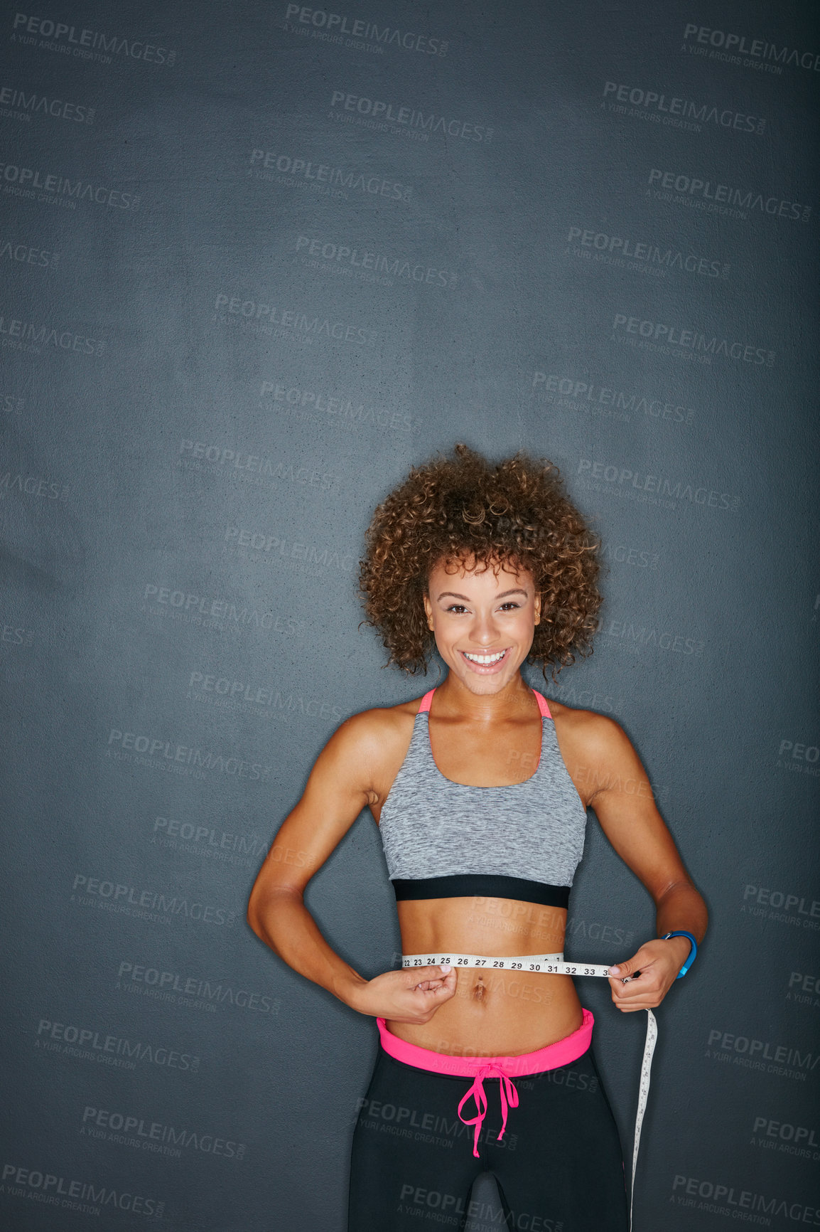 Buy stock photo Portrait of a sporty young woman measuring her waist against a grey background