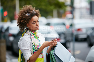 Buy stock photo Shot of an attractive young woman sending a text while on a shopping spree in the city