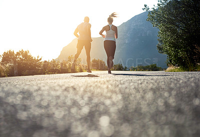 Buy stock photo Low angle shot of two people running on a tarmac road