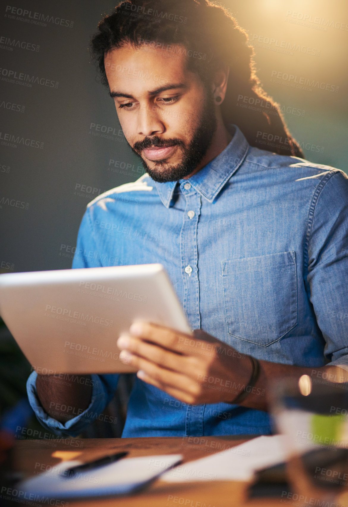 Buy stock photo Cropped shot of a young designer working late on a digital tablet in an office