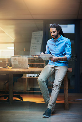 Buy stock photo Shot of a young designer working late on a digital tablet in an office