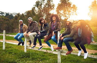 Buy stock photo Shot of a happy group of friends sitting in a row on a fence together