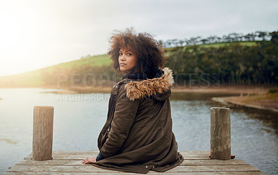 Buy stock photo Portrait of a young woman looking over her shoulder while sitting on a pier