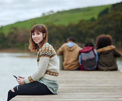 Buy stock photo Portrait of a young woman using her cellphone while sitting on the pier at a lake