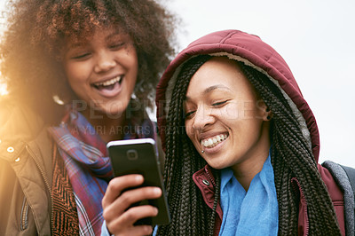 Buy stock photo Shot of a young woman showing her friend something on her cellphone while they stand outside