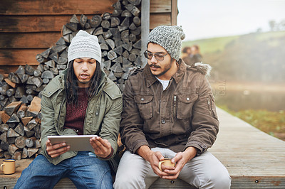 Buy stock photo Shot of a young man showing his friend something on his tablet while they spend the day outdoors