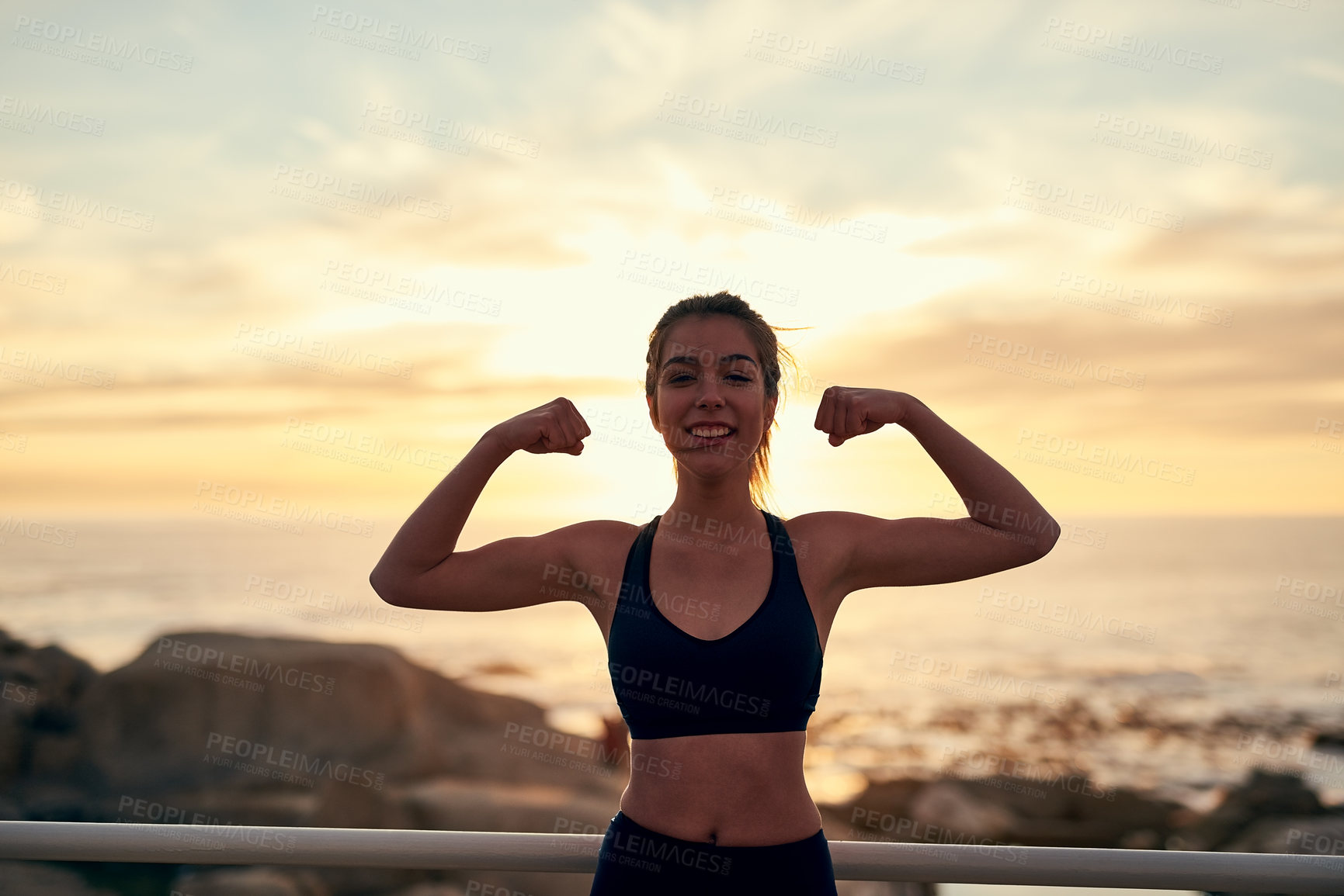 Buy stock photo Sunset, woman and flexing at beach for fitness, exercise and freedom in summer. Female runner, celebration and athlete in nature for workout, marathon training and ocean with achievement for portrait