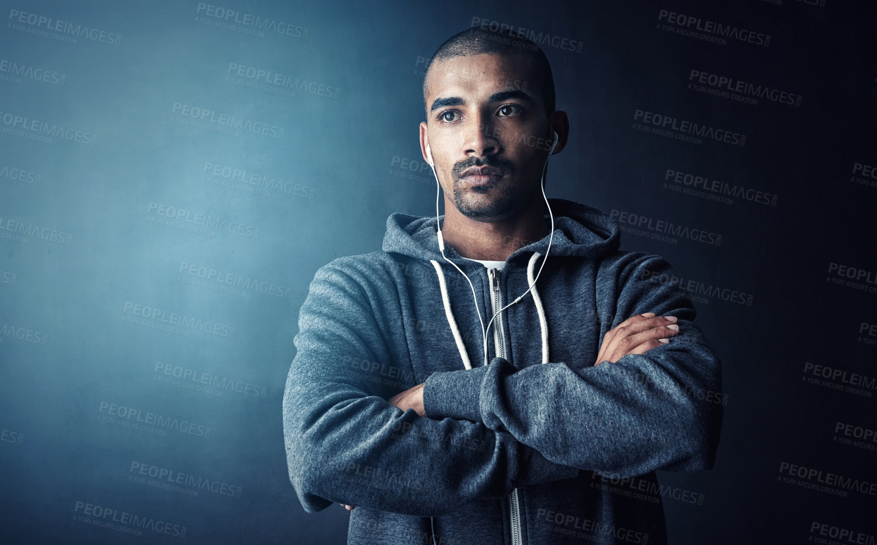 Buy stock photo Studio shot of a young man standing with his arms folded against a dark background