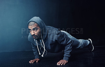 Buy stock photo Studio shot of a young man doing pushups against a dark background