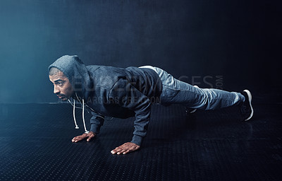 Buy stock photo Studio shot of a young man doing pushups against a dark background