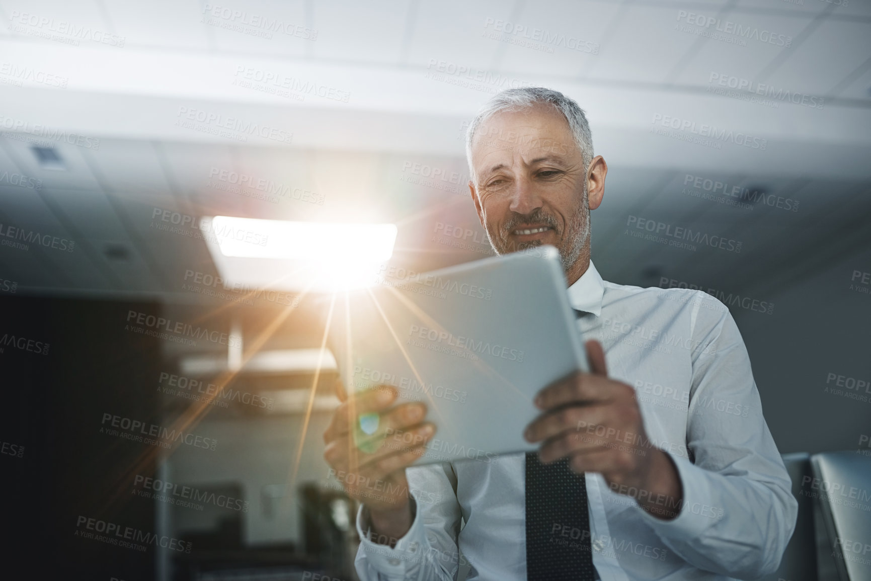 Buy stock photo Shot of a businessman standing in an office using a digital tablet