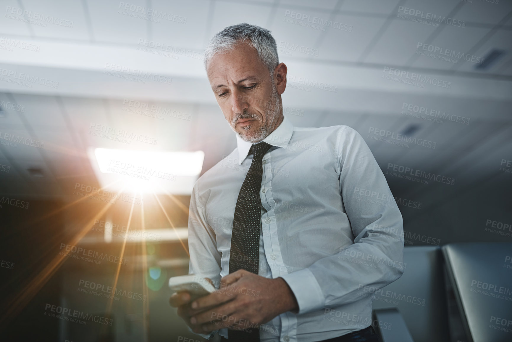 Buy stock photo Shot of a businessman standing in an office texting on a cellphone