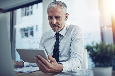 Buy stock photo Shot of a businessman sitting at his desk using a digital tablet
