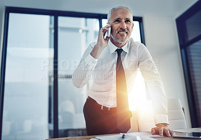 Buy stock photo Shot of a businessman standing in an office talking on a cellphone