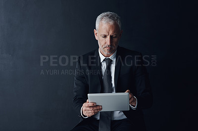 Buy stock photo Studio shot of a mature businessman using a digital tablet against a dark background