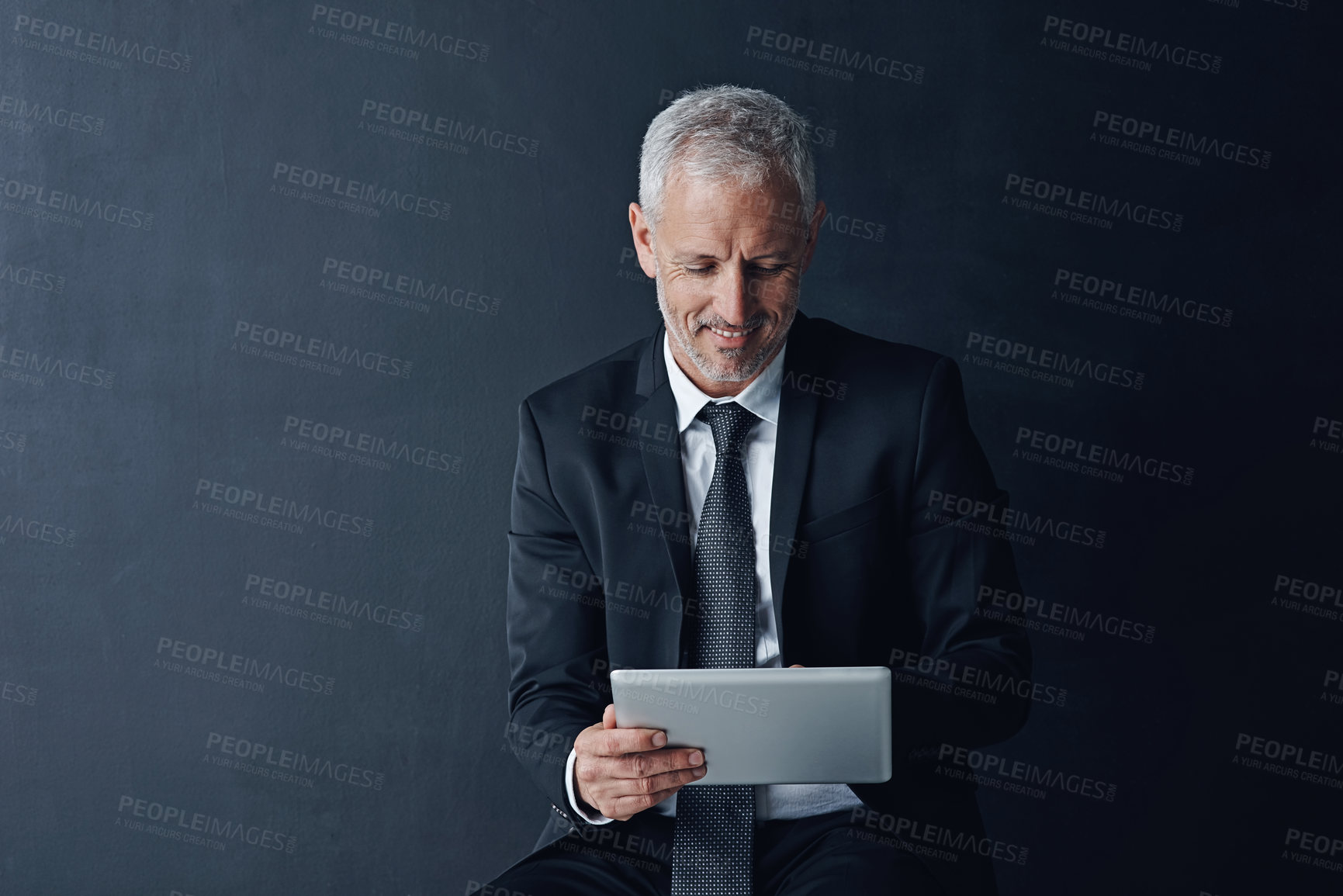 Buy stock photo Studio shot of a mature businessman using a digital tablet against a dark background