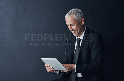 Buy stock photo Studio shot of a mature businessman using a digital tablet against a dark background