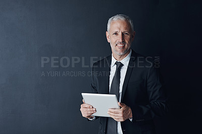 Buy stock photo Studio portrait of a mature businessman using a digital tablet against a dark background