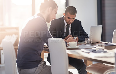 Buy stock photo Shot of two young businessmen using their smartphones at work