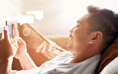 Buy stock photo Shot of a happy young man using his cellphone while lying on the couch at home