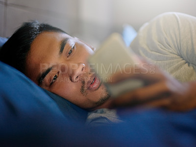 Buy stock photo Shot of a young man looking at his phone while lying in bed